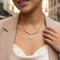 Collier Églantine doré avec perles blanches et pendentif fleur, porté sur une tenue élégante en extérieur
