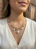 Collier Vaya doré à maillons avec médaillons martelés et perles blanches porté sur un haut blanc