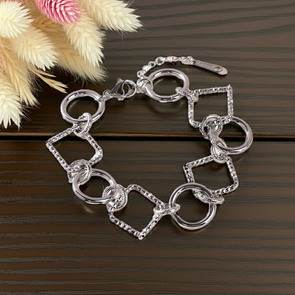 Bracelet Lizia argenté à maillons ronds et carrés sur une surface en bois foncé avec des fleurs séchées