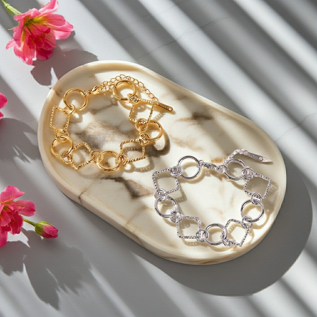 Bracelets Lizia doré et argenté à maillons ronds et carrés sur un plateau en marbre avec des fleurs roses