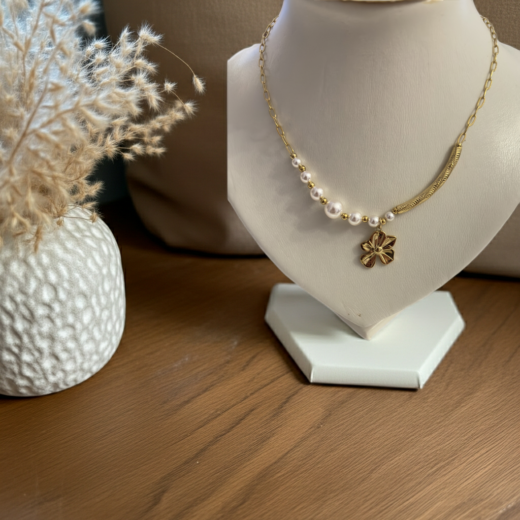 Collier Églantine doré avec perles blanches et pendentif fleur présenté sur un buste blanc près de fleurs séchées