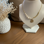 Collier Églantine doré avec perles blanches et pendentif fleur présenté sur un buste blanc près de fleurs séchées