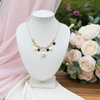 Collier Vaya doré à maillons avec médaillons martelés et perles blanches présenté sur un buste blanc entouré de fleurs roses et blanches